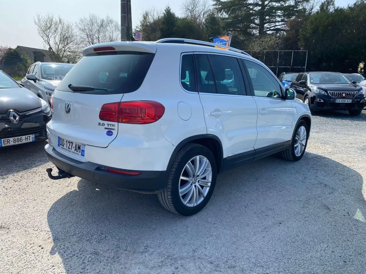 Volkswagen Tiguan blanc vu en 3/4 arrière droit avec attelage et jantes alliage 18 pouces sur parking.