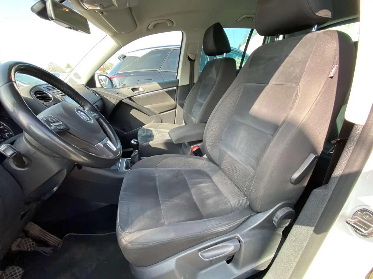 Intérieur avant droit du Volkswagen Tiguan blanc 2014, sièges tissu noir et volant cuir multifonction visible.