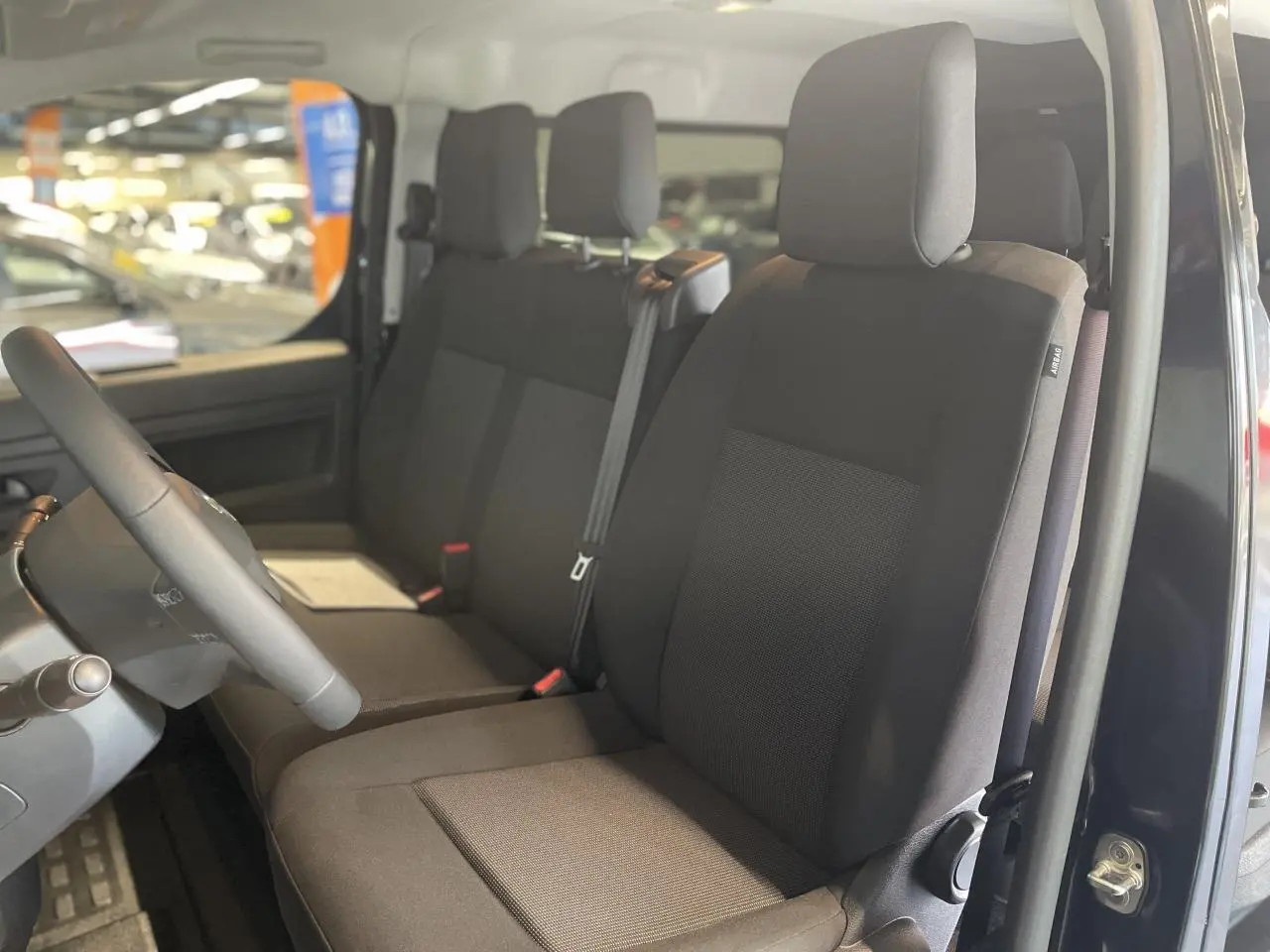 Vue intérieure côté conducteur du double cabine Opel Vivaro 2025 noir carbone, sièges tissu bi-ton noir/gris avec appuie-têtes.
