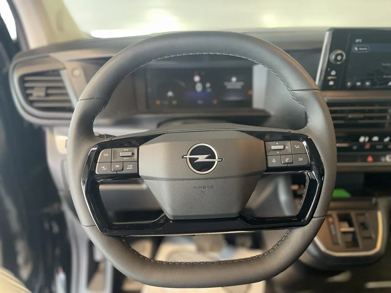 Gros plan sur le volant noir de l'Opel Vivaro 2025 avec commandes intégrées et tableau de bord numérique flou en arrière-plan.