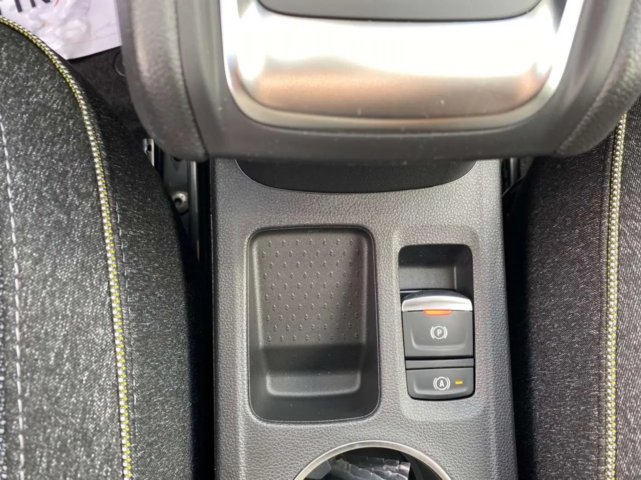 Gros plan sur la console centrale du Renault Captur Techno 2025, montrant le frein à main électrique et un espace de rangement.