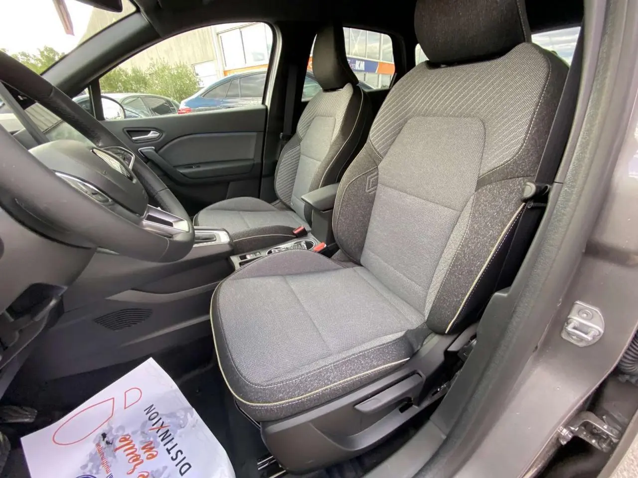 Vue intérieure côté conducteur du Renault Captur 2025, sièges tissu gris avec surpiqûres jaunes, volant et console visibles.