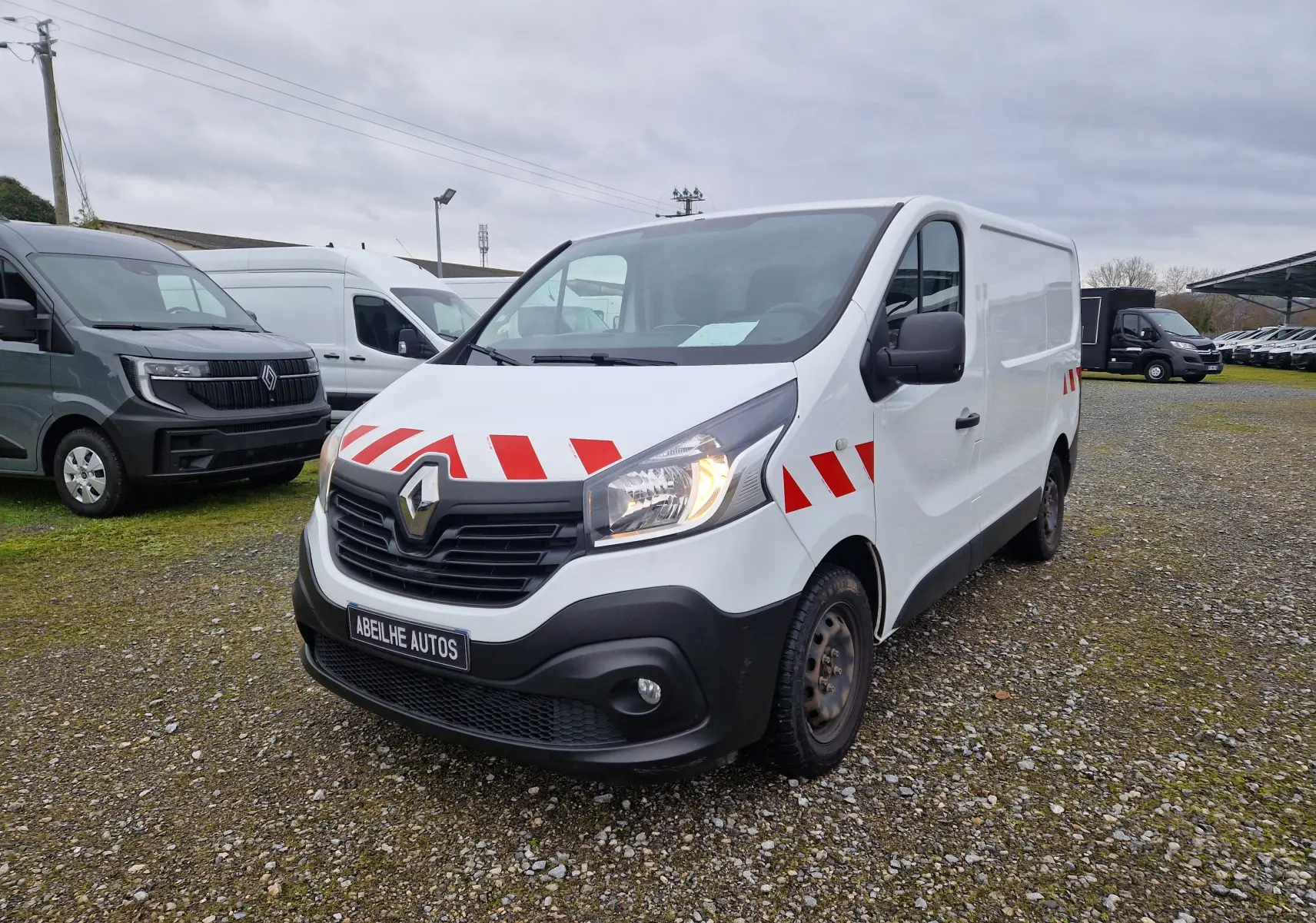 Vue 3/4 avant d’un Renault Trafic fourgon blanc 2019 avec bandes rouges réfléchissantes sur capot et portières.