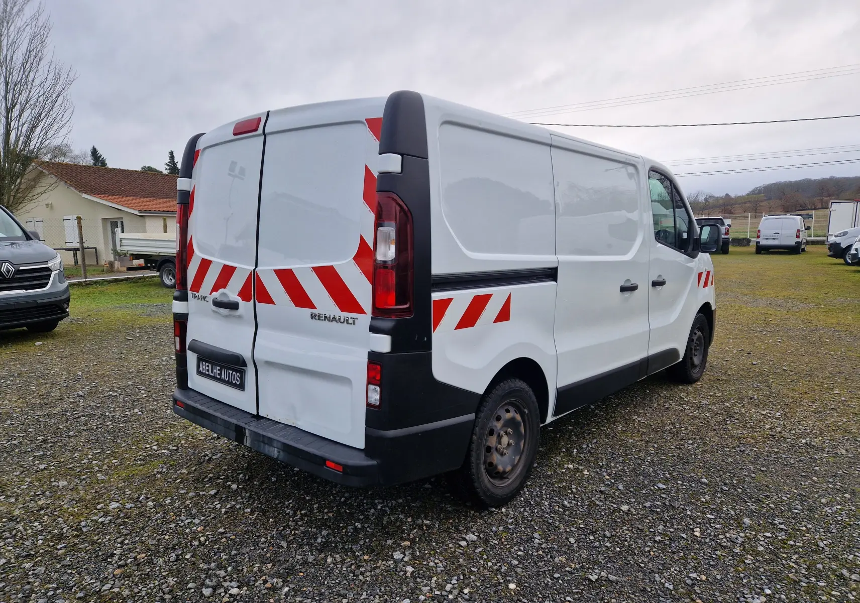 Renault Trafic Fourgon blanc vu en 3/4 arrière droit avec bandes rouges réfléchissantes sur portes et flanc.
