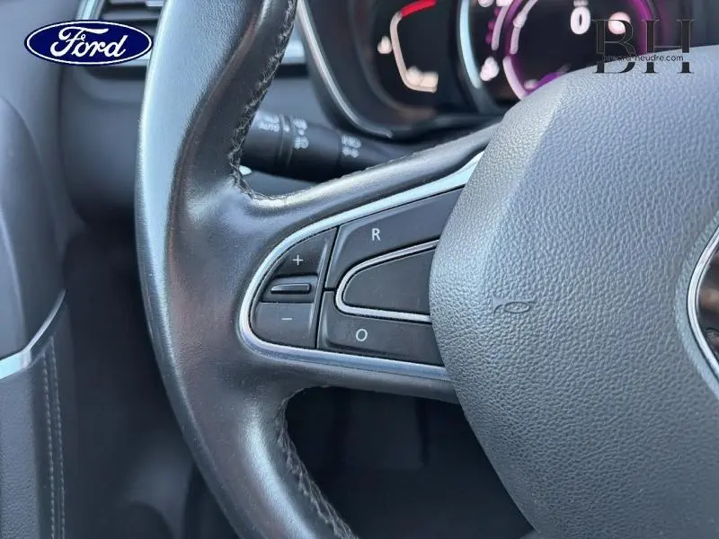 Gros plan sur le volant cuir noir avec commandes intégrées, tableau de bord flou en arrière-plan.