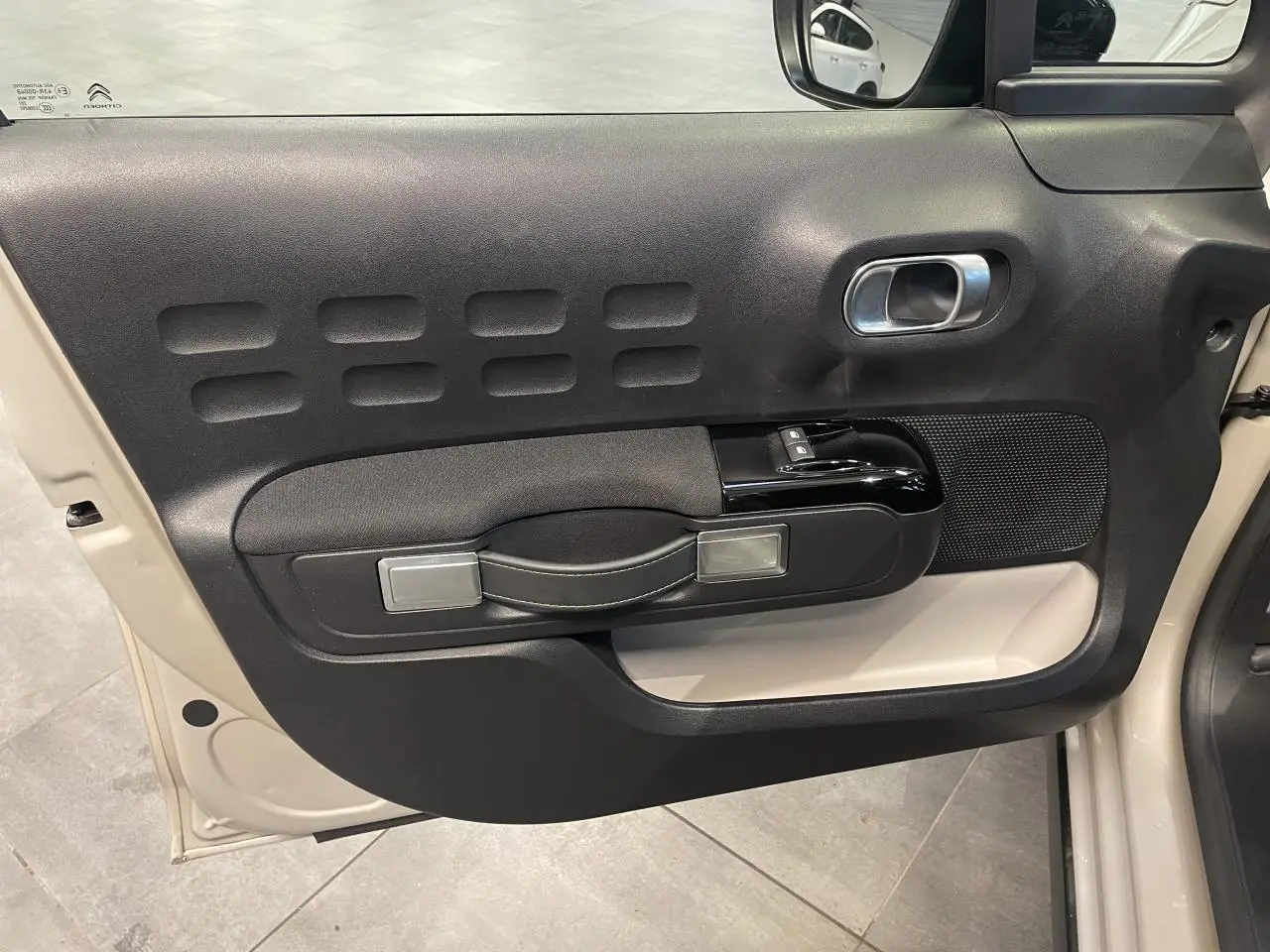 Vue intérieure côté gauche de la porte beige clair d'une Citroën C3 2024 avec accoudoir textile noir et poignée argentée.
