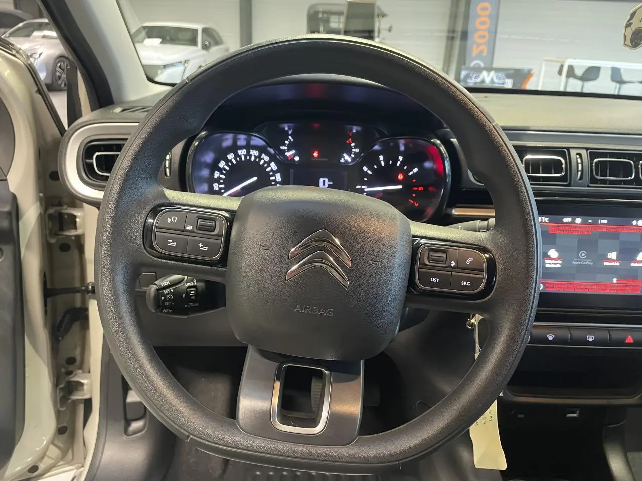 Vue intérieure centrée sur le volant noir de la Citroën C3 beige clair avec tableau de bord et écran tactile visible.