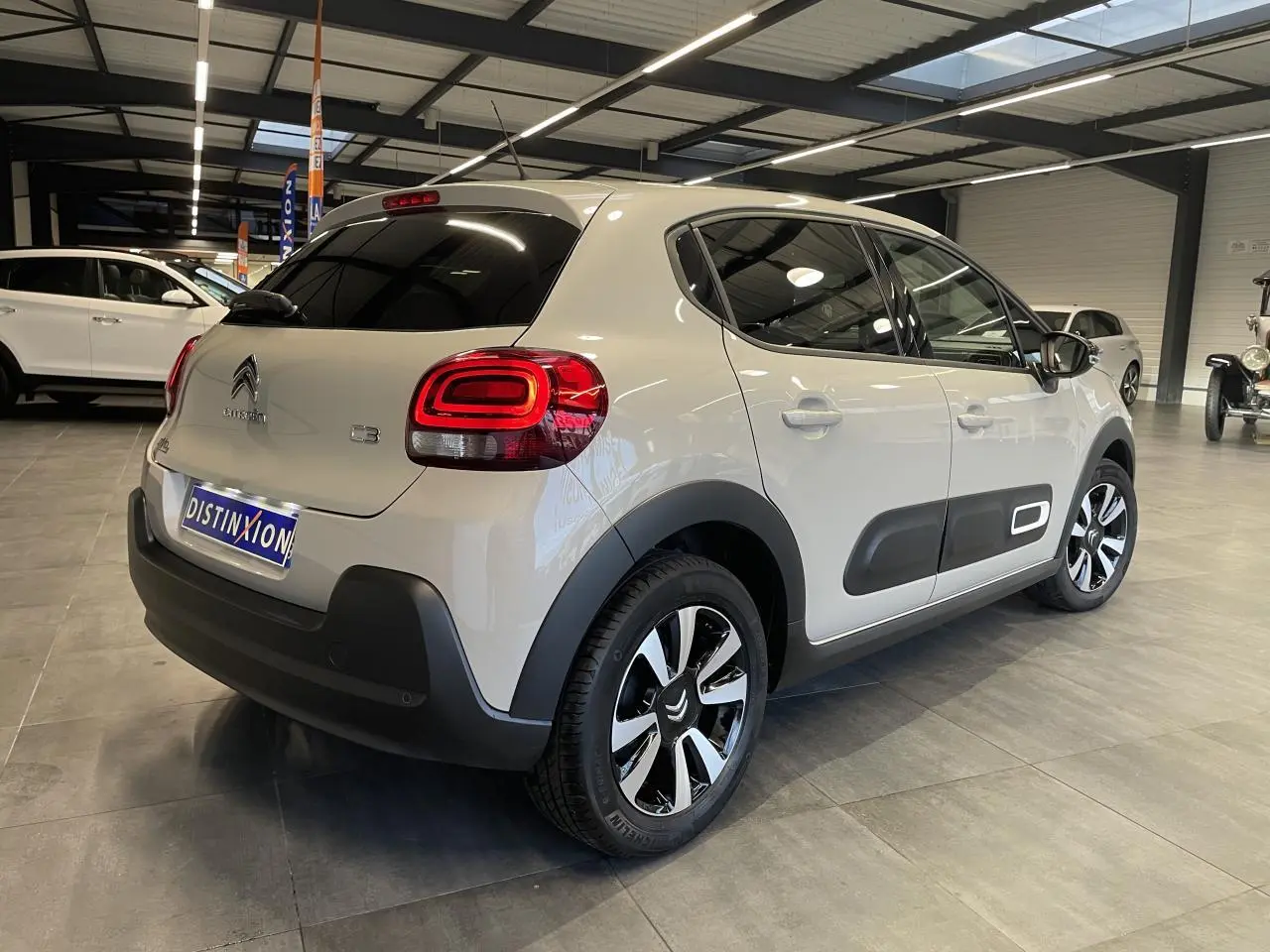 Vue 3/4 arrière droite d'une Citroën C3 beige clair avec Airbump noirs et jantes alliage diamantées en showroom.