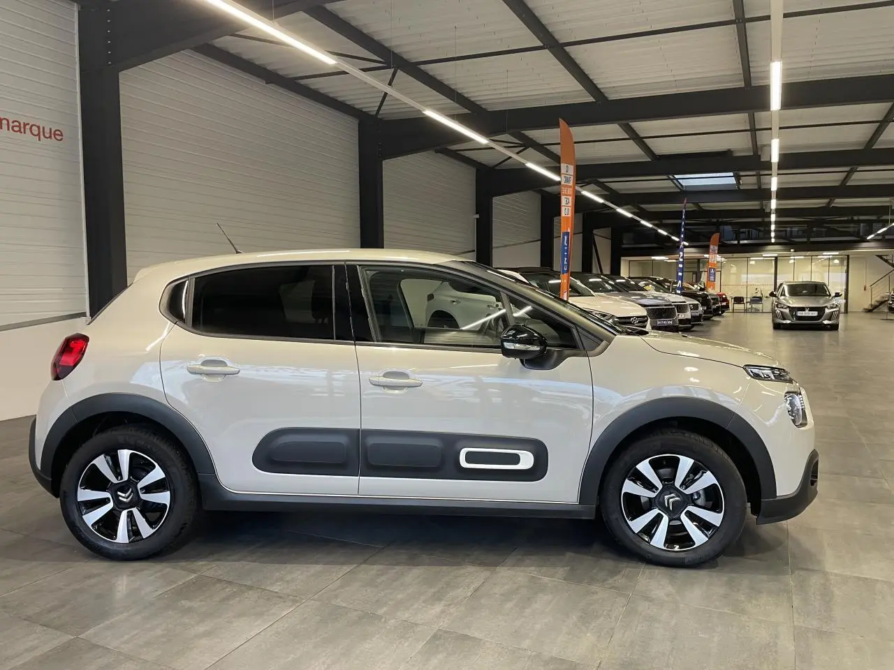 Vue de profil côté gauche d'une Citroën C3 beige clair avec Airbump noirs et jantes alliage diamantées en showroom.