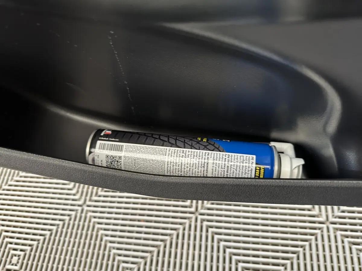 Gros plan sur une bombe aérosol rangée dans la porte intérieure d'une Aixam Ambition 0.5 City Pack bleu.