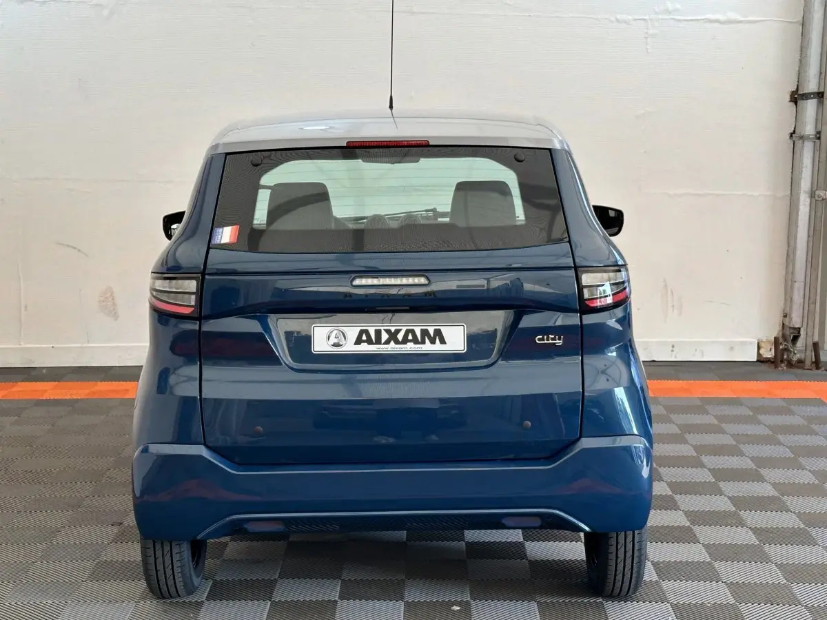 Vue arrière d'une AIXAM Ambition 0.5 City Pack bleu 2026 avec plaque et vitres teintées, stationnée en intérieur.