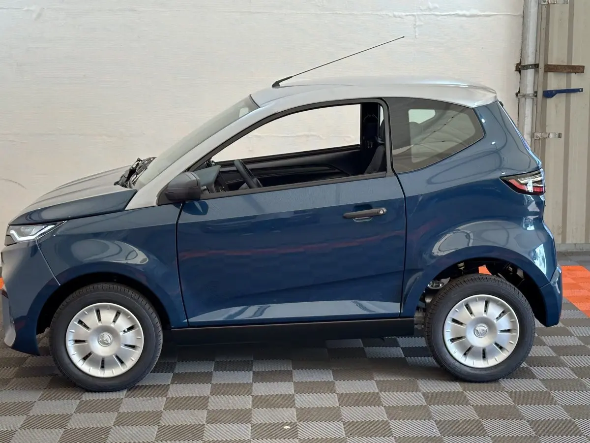 Profil gauche d'une Aixam Ambition 0.5 City Pack 2026 bleu avec toit gris et rétroviseur caméra côté conducteur.