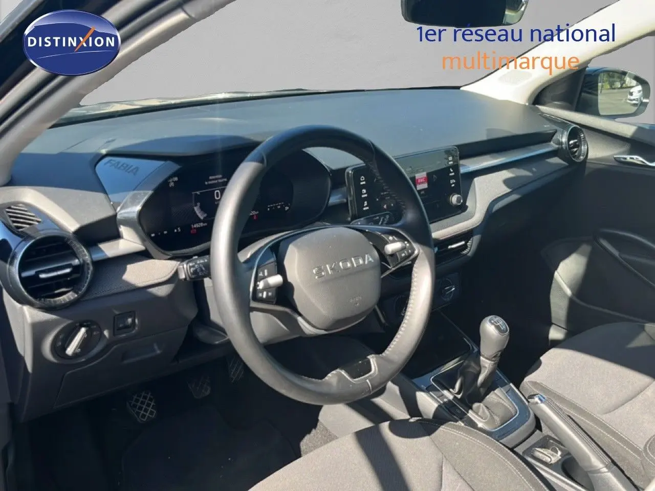 Vue intérieure côté conducteur de la Skoda Fabia 2025, tableau de bord noir avec volant multifonction et levier de vitesse manuel.
