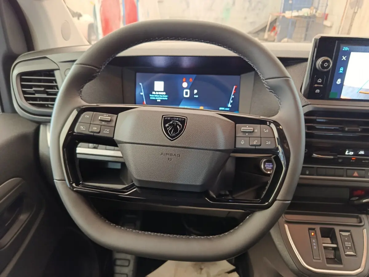 Vue rapprochée du volant noir multifonctions de la Peugeot Expert Fourgon XL avec tableau de bord digital en arrière-plan.