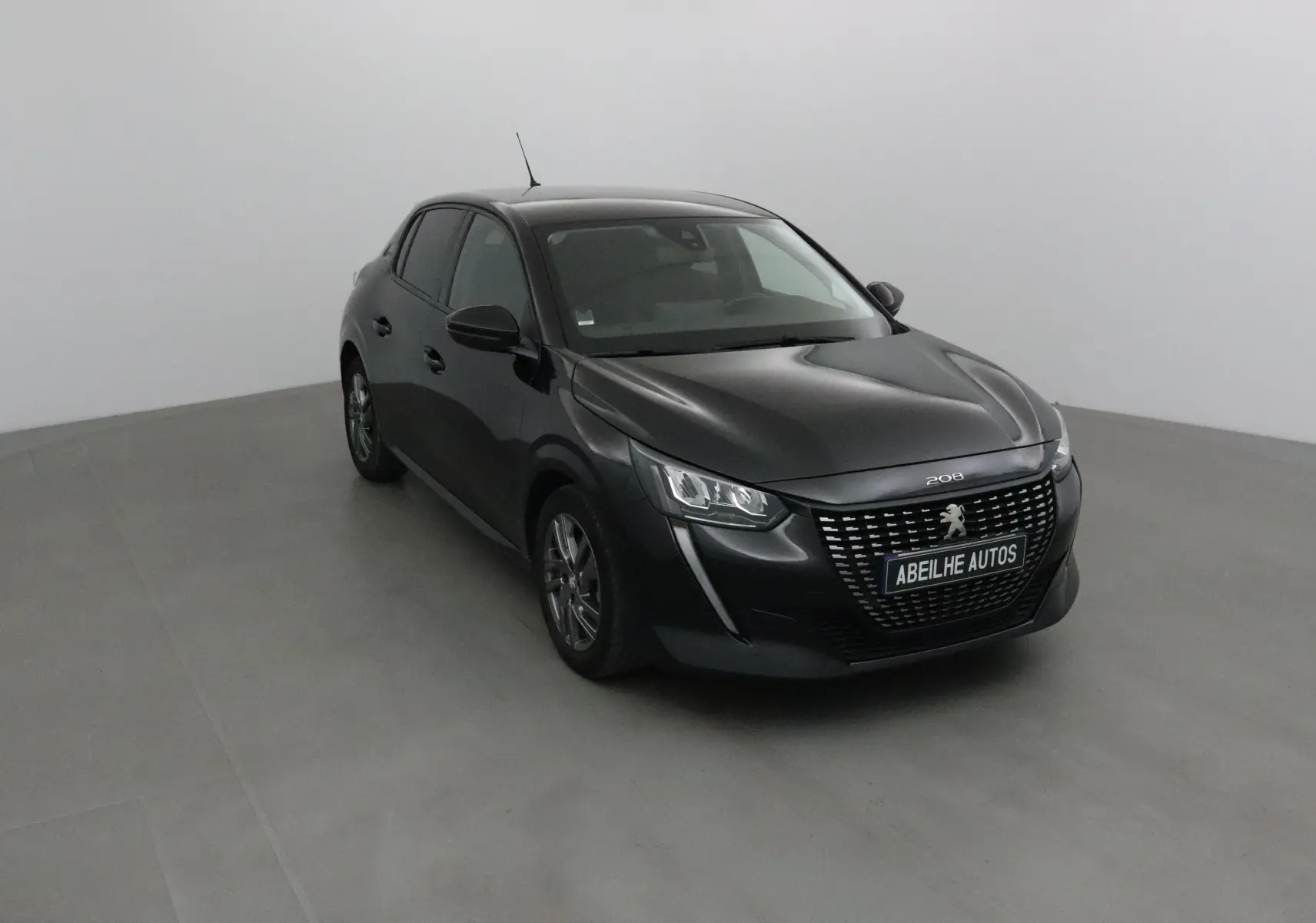 Peugeot 208 noire vue en 3/4 avant droit dans un studio, avec calandre distinctive et jantes alliage.