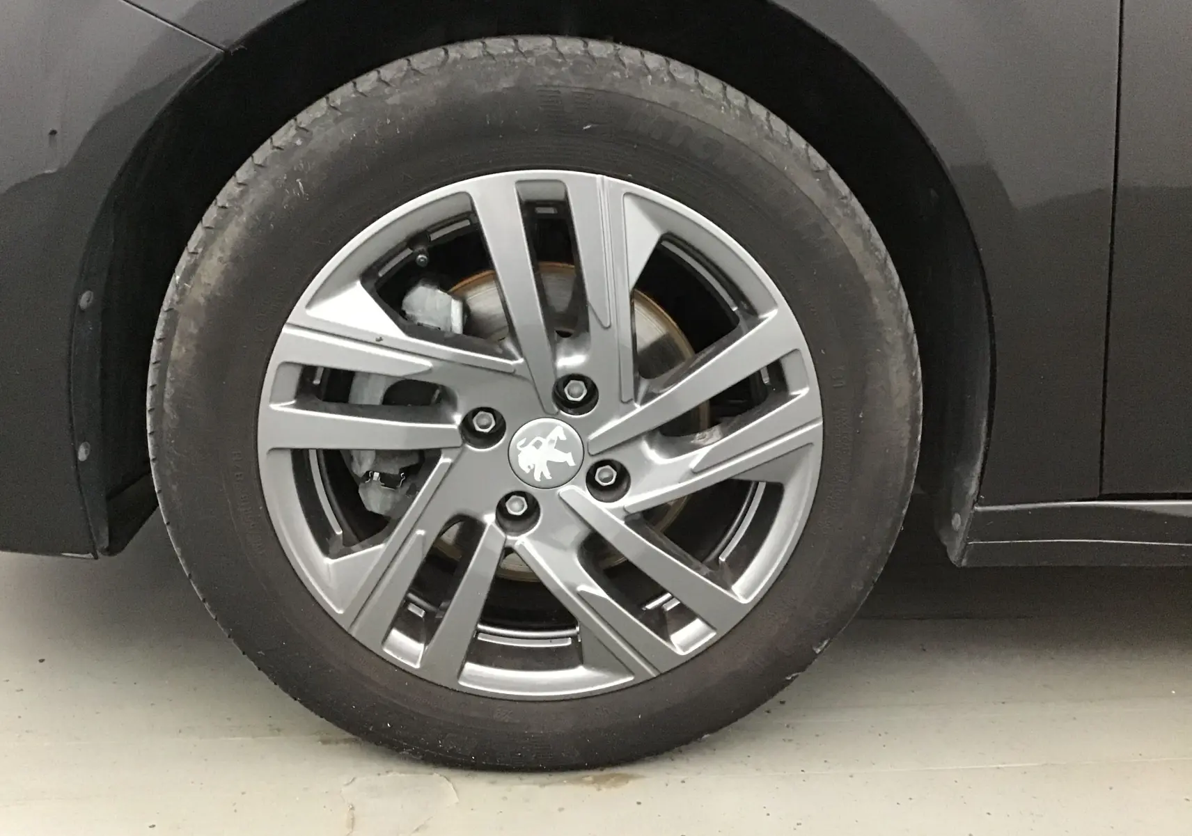 Gros plan sur la roue avant gauche d'une Peugeot 208 noire 2022 avec jante alliage gris et logo lion central.