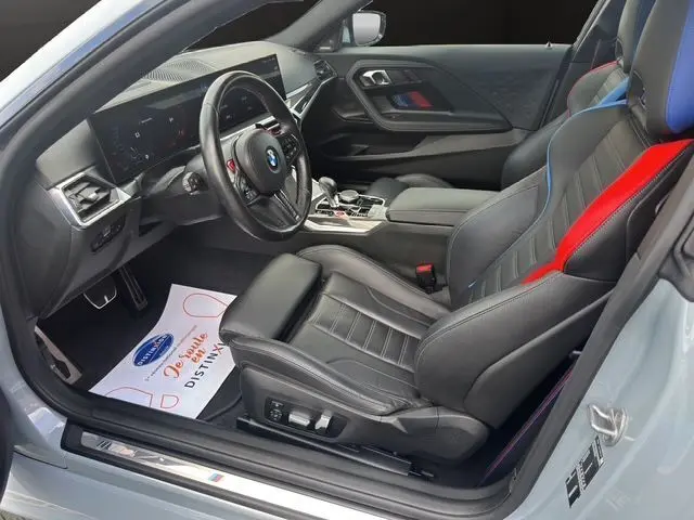 Intérieur côté conducteur d'une BMW M2 G87 gris Brooklyn avec sièges sport noirs et accents bleus et rouges.