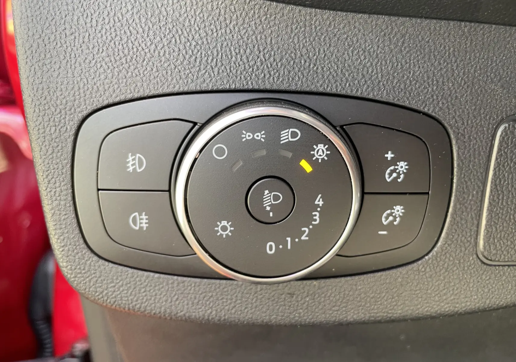 Gros plan sur le bouton de réglage des phares dans l'habitacle du Ford Puma rouge, avec indicateur lumineux allumé.