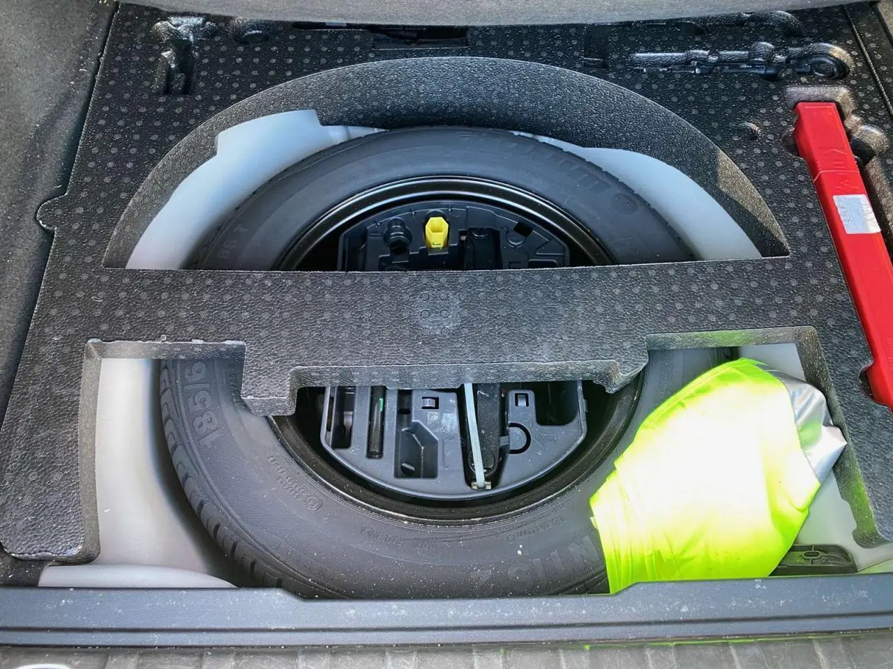 Vue rapprochée de la roue de secours en tôle noire dans le coffre du Peugeot 2008 2019 avec un gilet jaune visible.