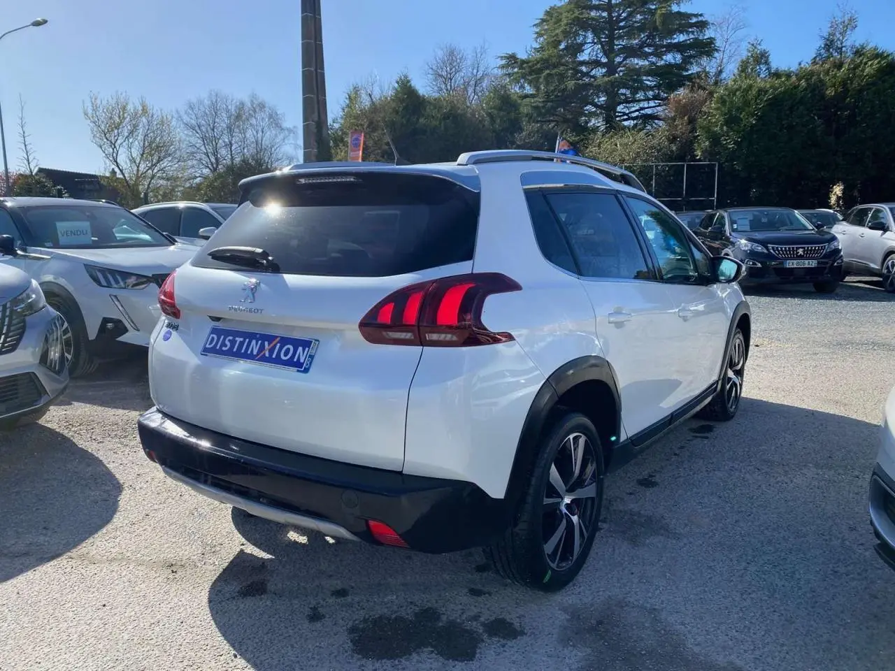 Vue 3/4 arrière droite d'un Peugeot 2008 blanc avec jantes aluminium 17'' et toit vitré panoramique en extérieur.