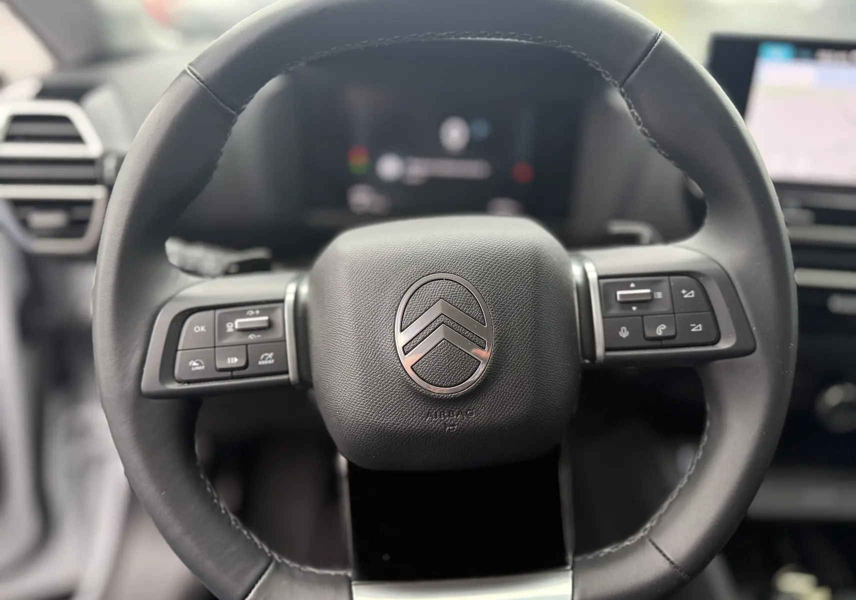 Gros plan sur le volant cuir noir du Citroën C4 Hybrid 145 e-DCS6 Max, avec commandes intégrées et tableau de bord flou en arrière-plan.