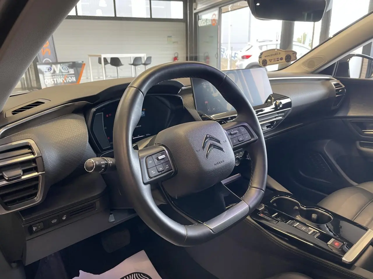 Vue intérieure du poste de conduite du Citroën C5 X 2024, volant cuir noir et écran tactile central visible.