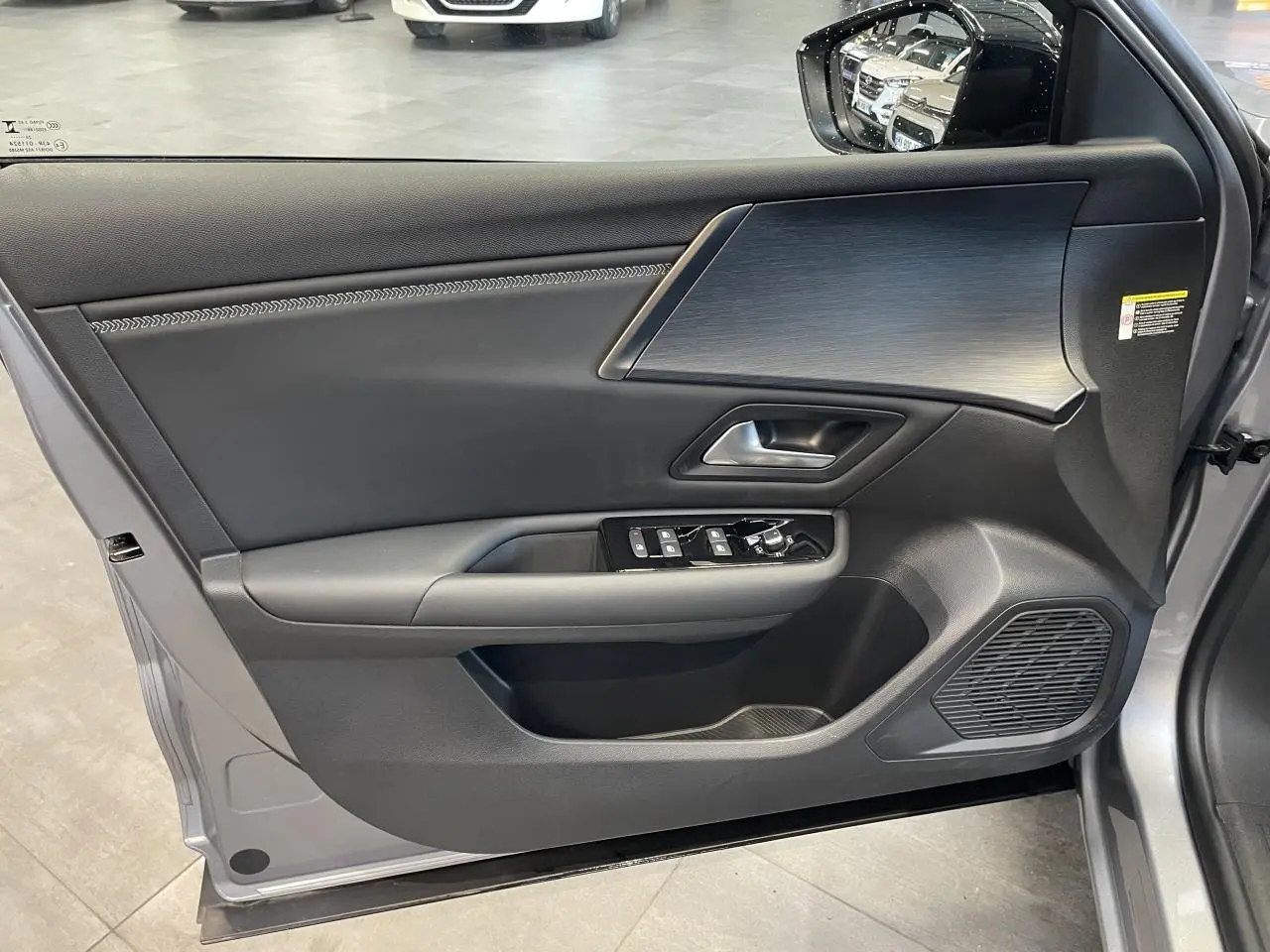 Vue intérieure côté gauche de la porte avant gris foncé du Citroën C5 X 2024 avec commandes de vitres et finition moderne.