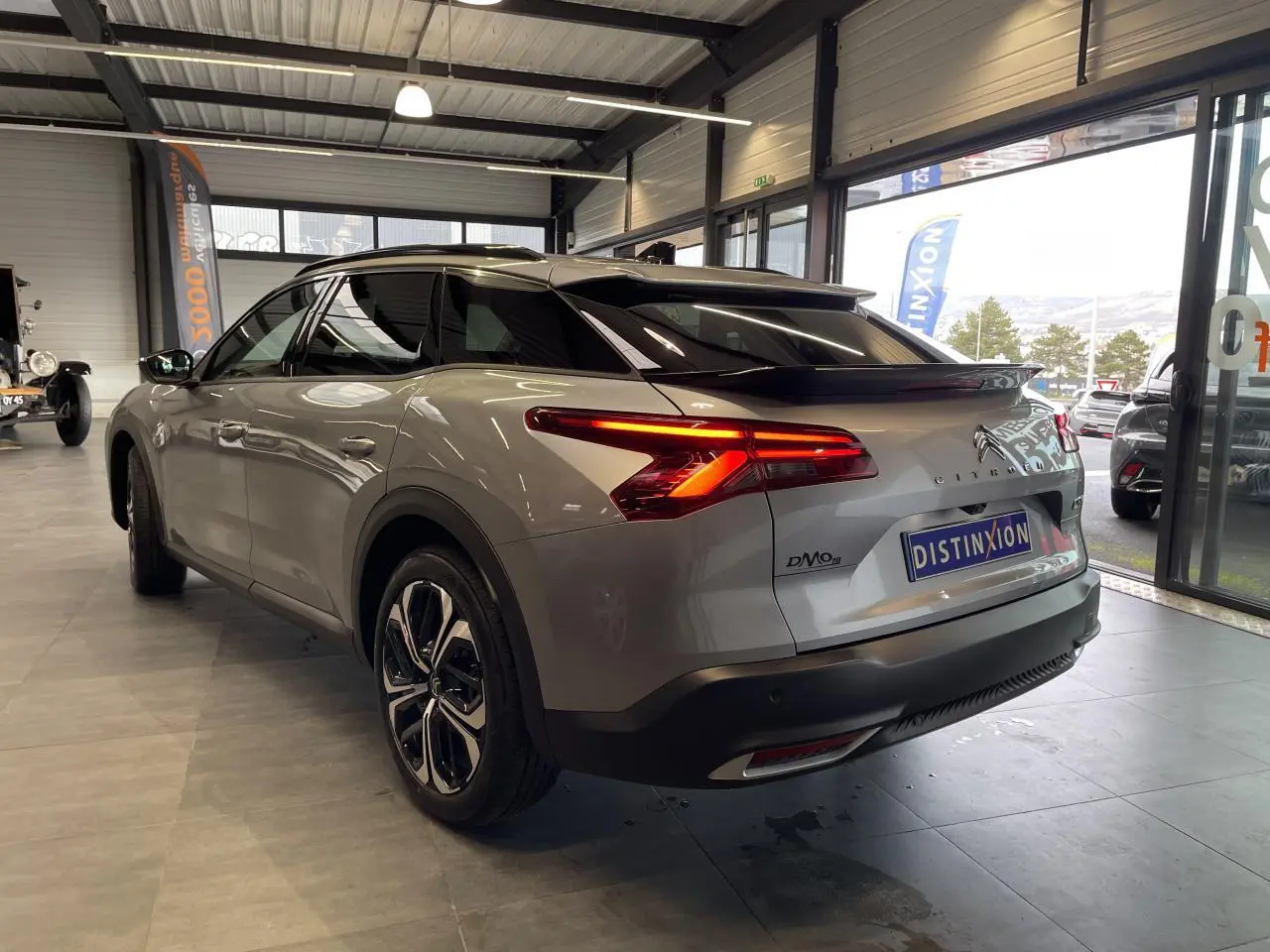 Vue 3/4 arrière droite d'une Citroën C5 X 2024 gris foncé avec feux arrière allumés dans un showroom.