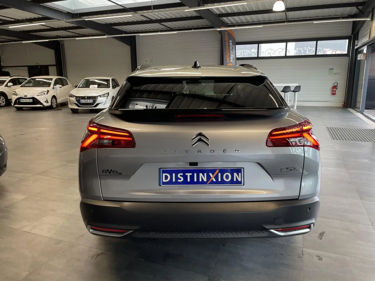 Vue arrière d'une Citroën C5 X gris foncé 2024 avec feux LED allumés dans un showroom intérieur.