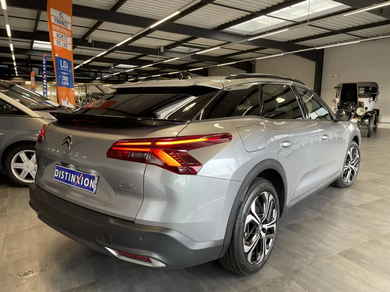 Vue 3/4 arrière droite d'une Citroën C5 X 2024 gris foncé avec feux arrière allumés en concession.