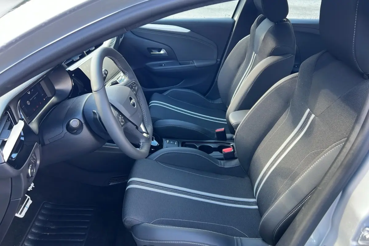 Vue intérieure côté conducteur de l’Opel Corsa Hybrid 2026, sièges tissu noir avec bandes grises et volant multifonctions.