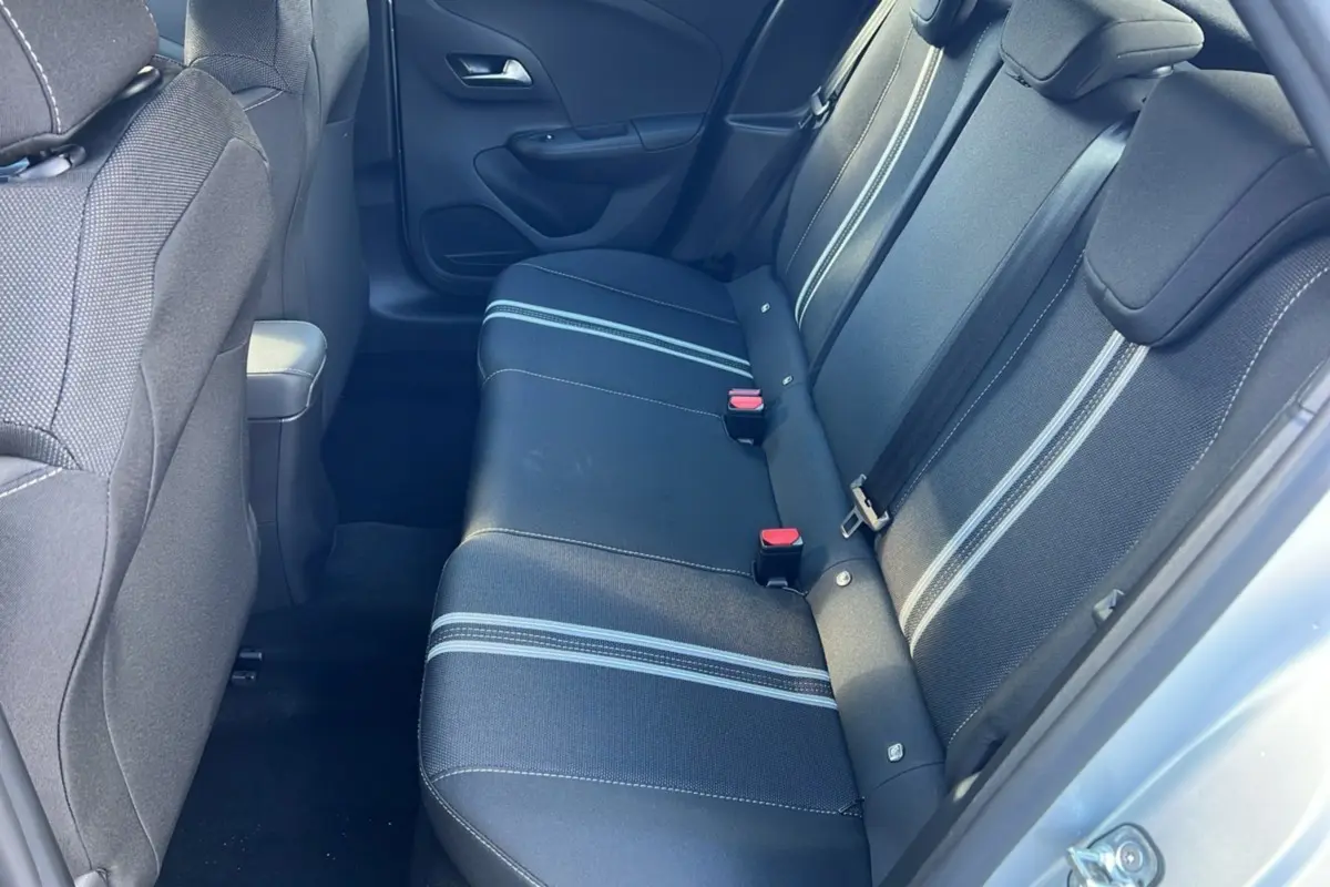 Vue intérieure côté arrière droit de l’Opel Corsa Hybrid 2026 avec banquette noire à bandes grises et ceintures visibles.