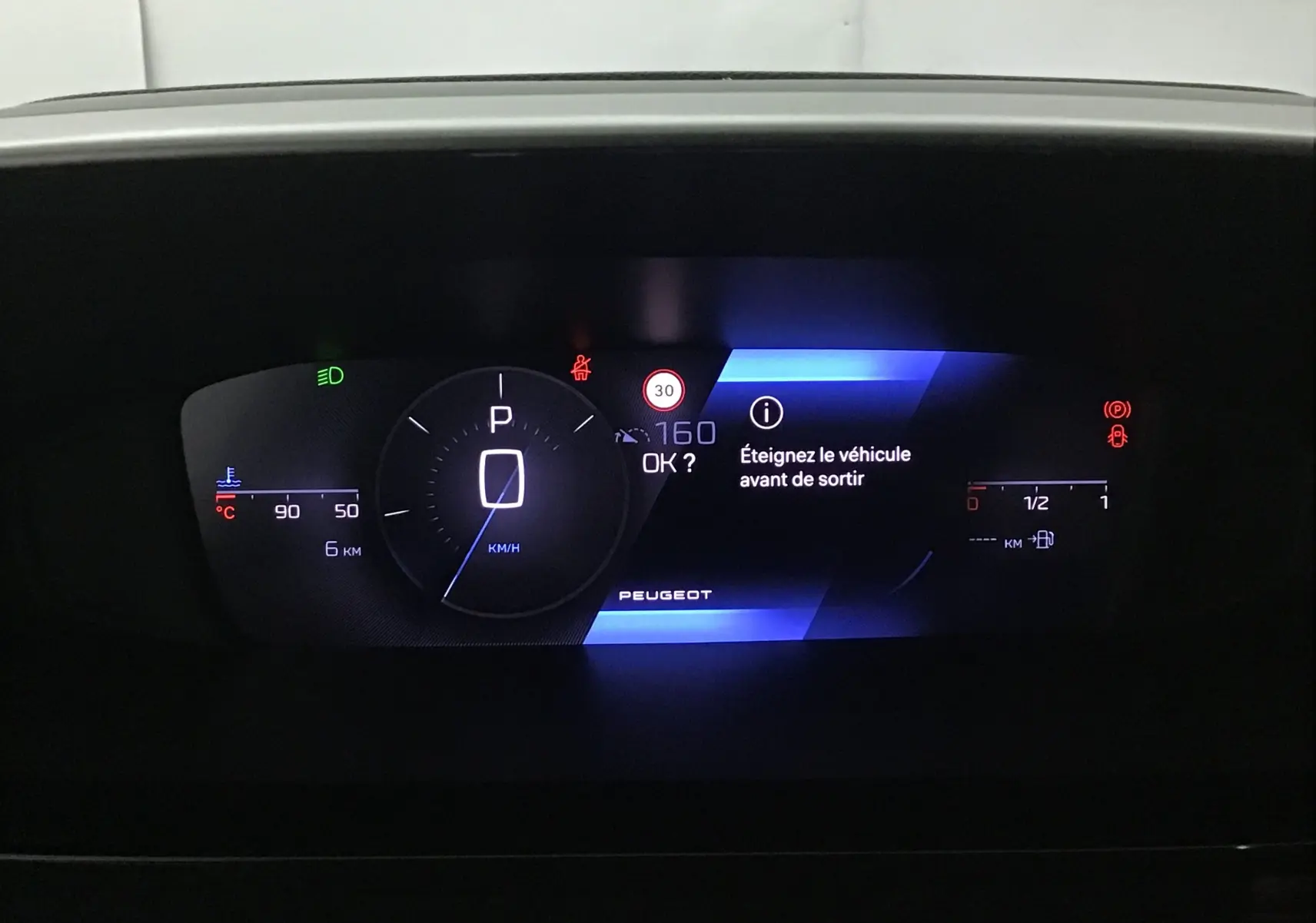 Tableau de bord numérique de Peugeot 308 2025 affichant vitesse, température moteur et message d'alerte.