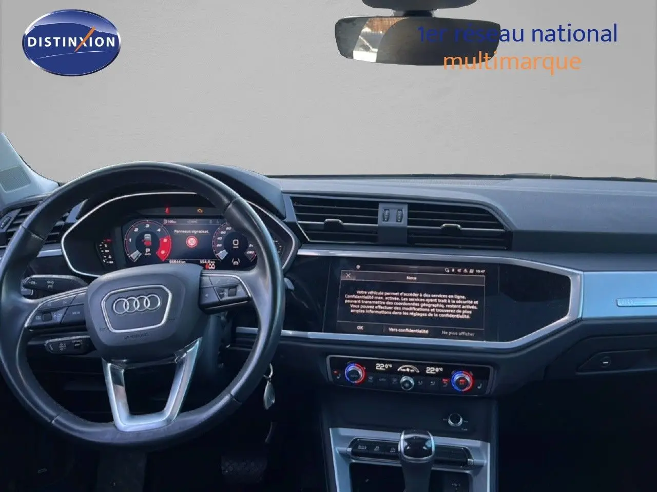 Vue intérieure de face du tableau de bord d’un Audi Q3 Sportback noir 2022, avec volant multifonction et écran tactile central.
