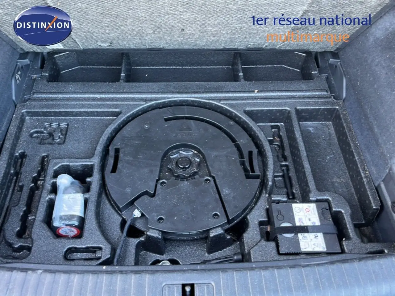 Coffre ouvert montrant le rangement noir avec kit de réparation et emplacement roue de secours de l'Audi Q3 Sportback noir.