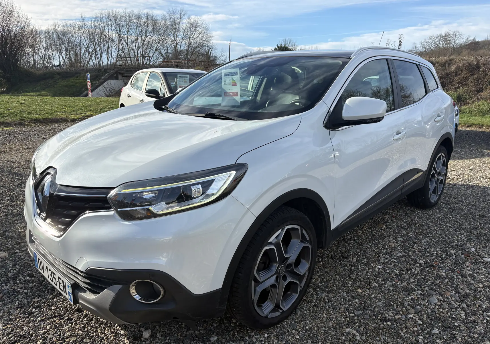 Renault Kadjar blanc vue 3/4 avant droit sur parking, avec jantes alliage distinctives et calandre noire.