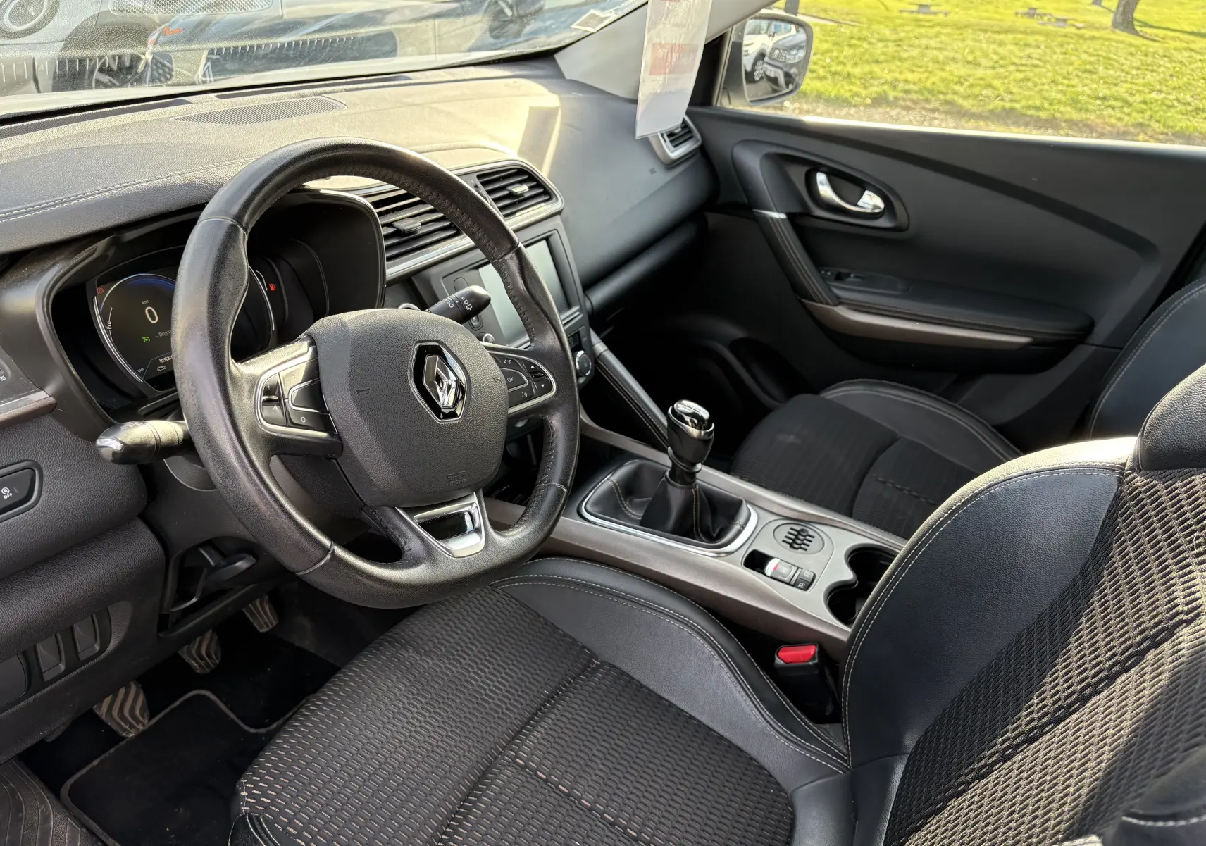 Vue intérieure côté conducteur du Renault Kadjar blanc 2015, mettant en valeur le volant, la boîte manuelle et la console centrale.