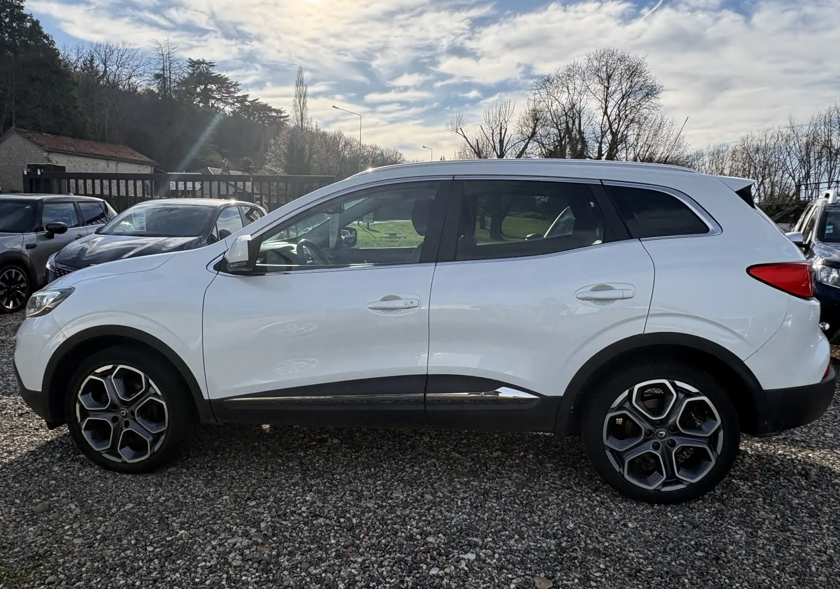Profil côté gauche d'un Renault Kadjar blanc 2015 avec jantes alliage et détails noirs sur les bas de caisse.