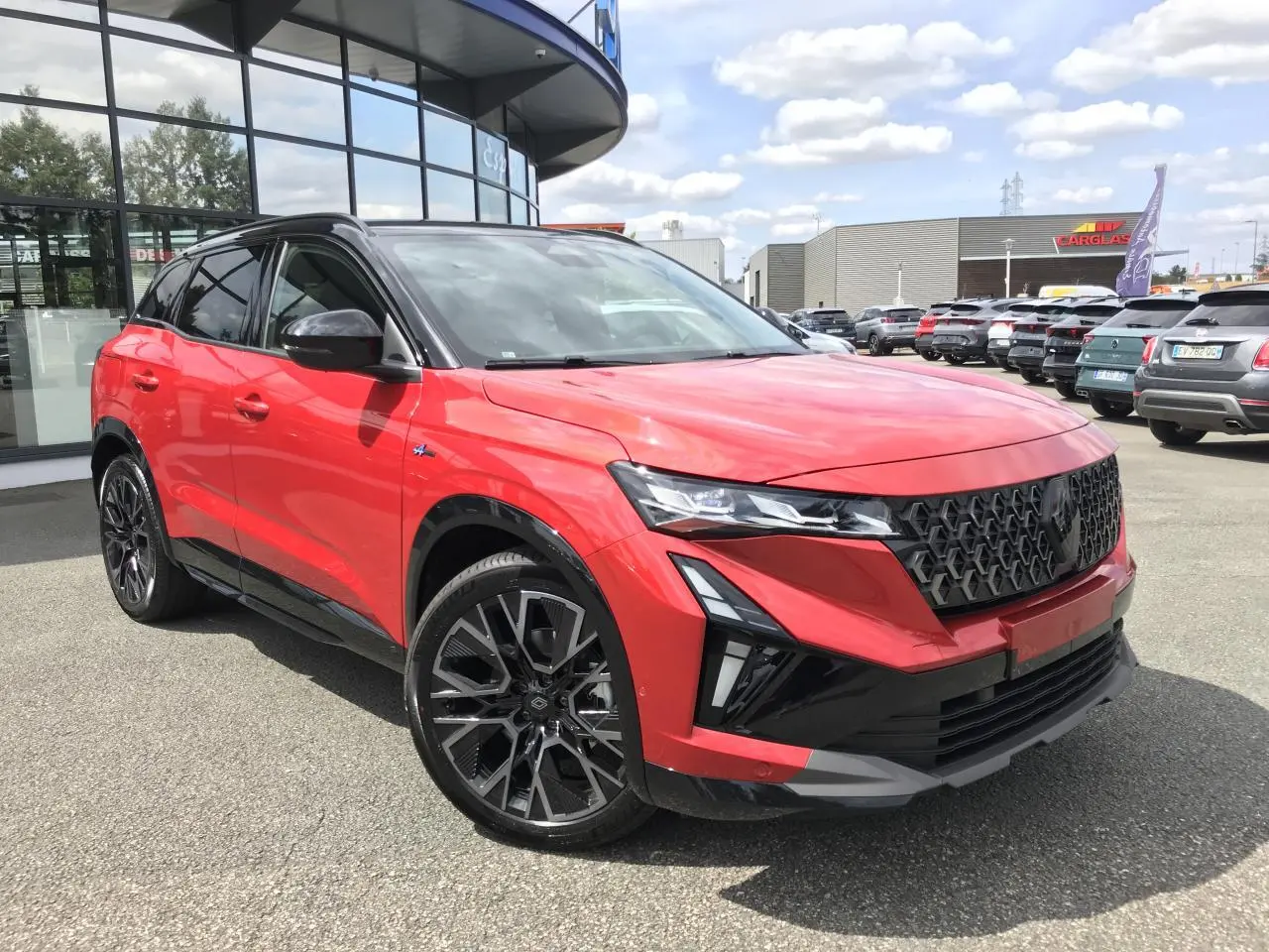 Renault Austral rouge et noir en 3/4 avant droit, avec jantes alliage noires et calandre imposante noire.