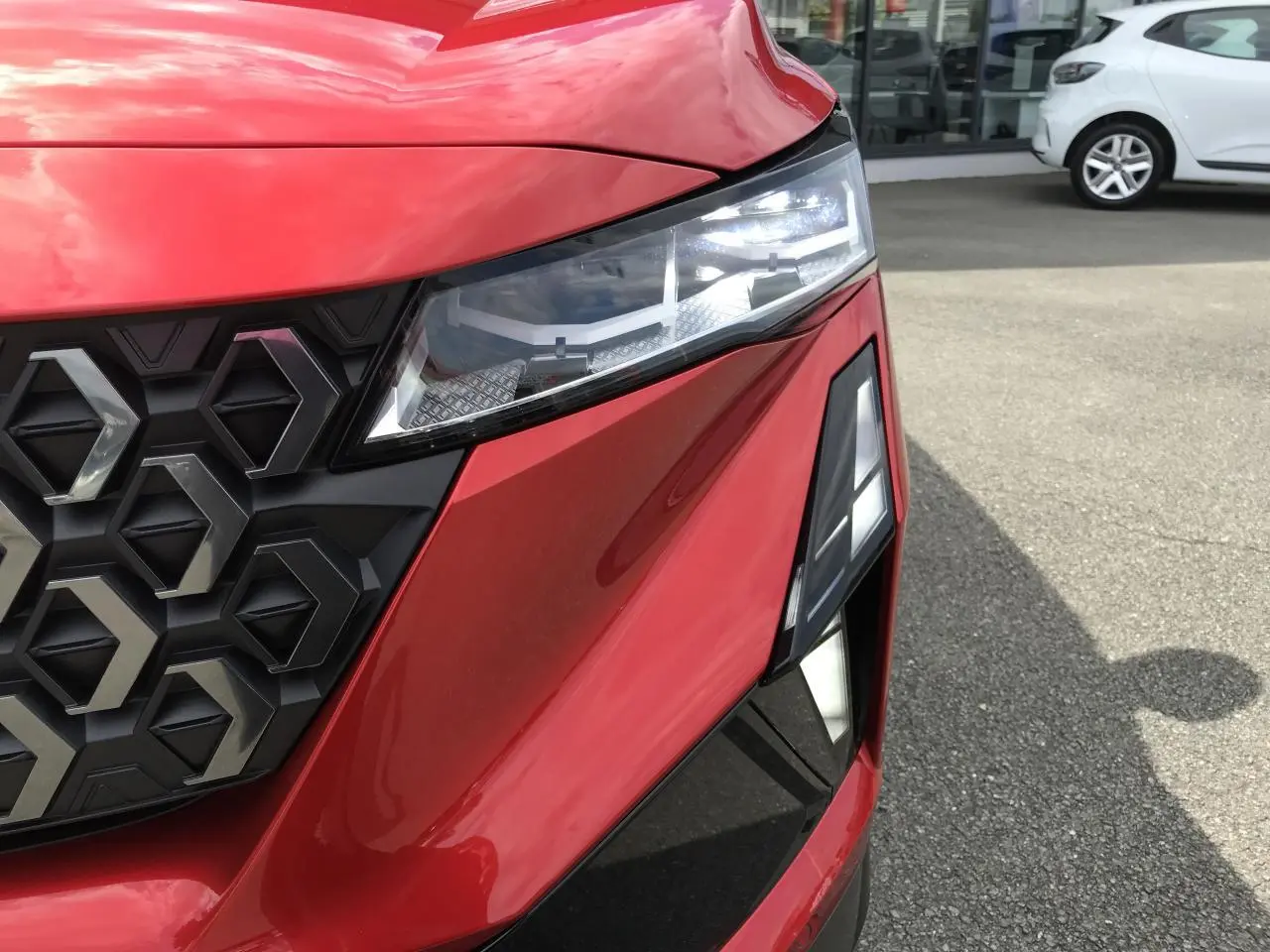 Gros plan sur l'avant droit rouge et noir du Renault Austral 2025 avec phares LED et calandre hexagonale distinctive.