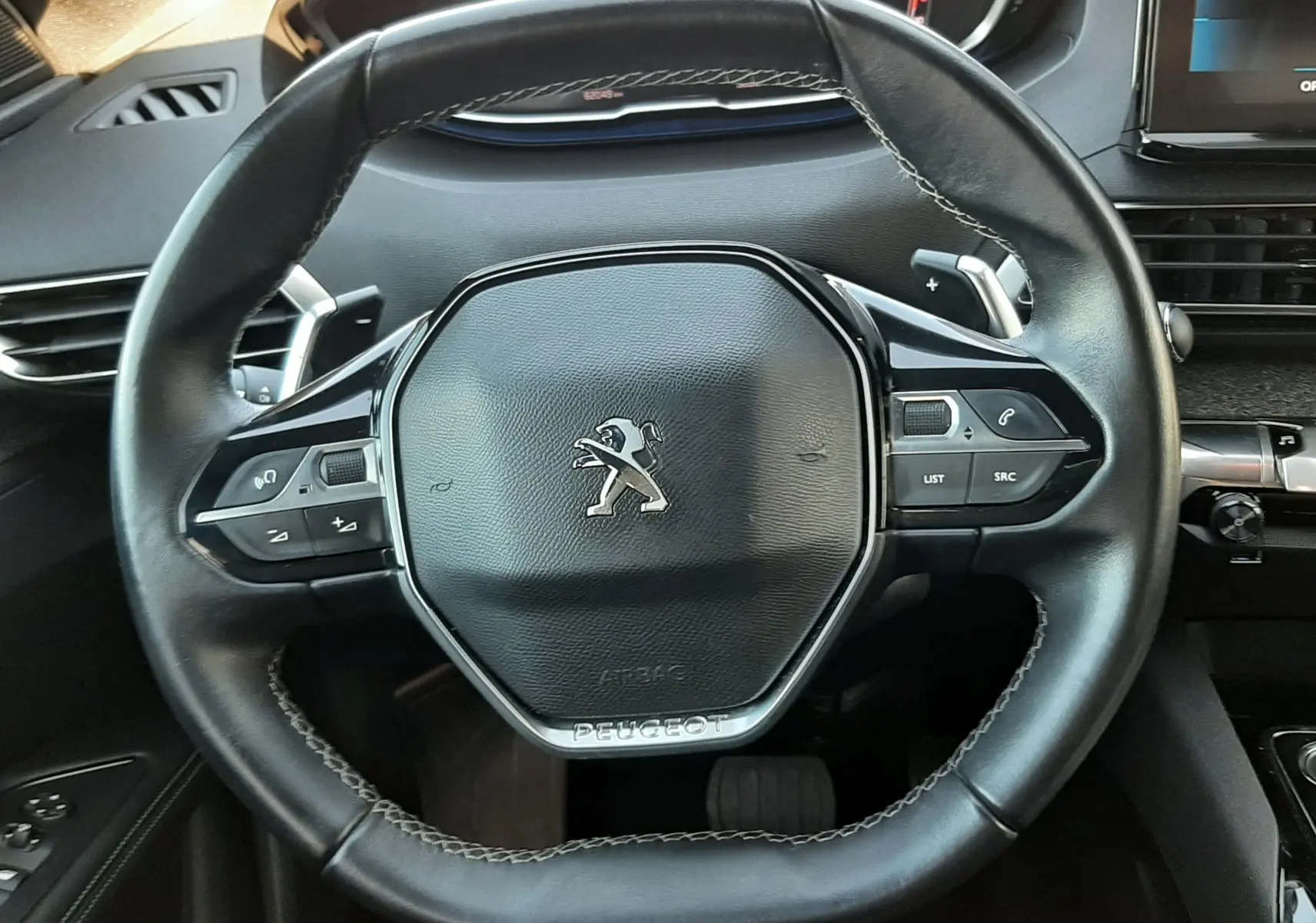 Vue rapprochée du volant cuir noir du Peugeot 3008 2023 avec commandes intégrées et tableau de bord numérique.
