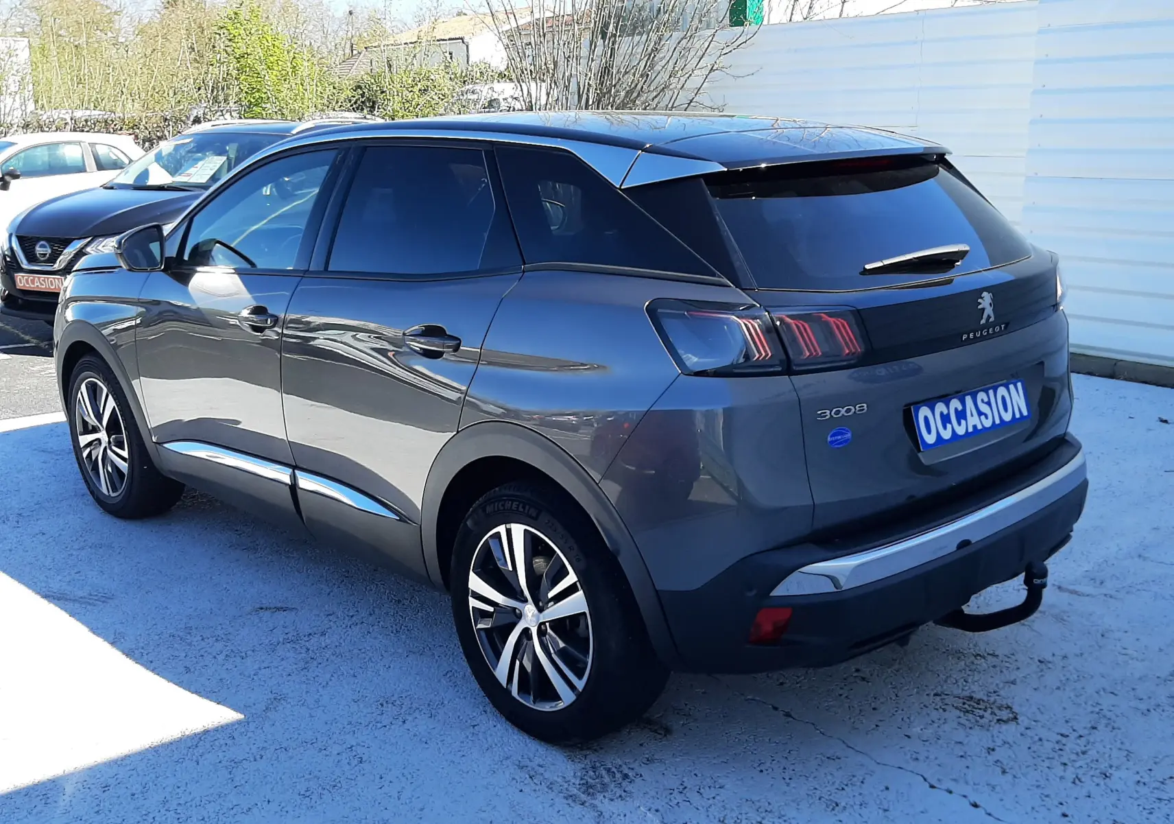 Vue 3/4 arrière droit d’un Peugeot 3008 gris platinium avec jantes alliage et badge BlueHDi, stationné en extérieur.