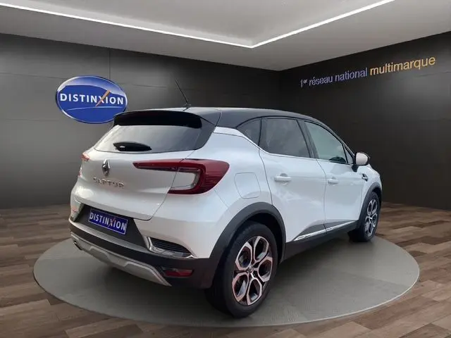 Vue 3/4 arrière droite du Renault Captur blanc nacré avec toit noir, jantes bi-ton et feux arrière LED dans un showroom.