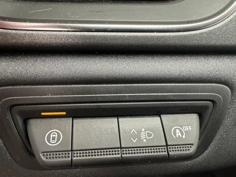 Gros plan sur les boutons de commande intérieurs noirs du Renault Captur 2025, avec témoin orange allumé.
