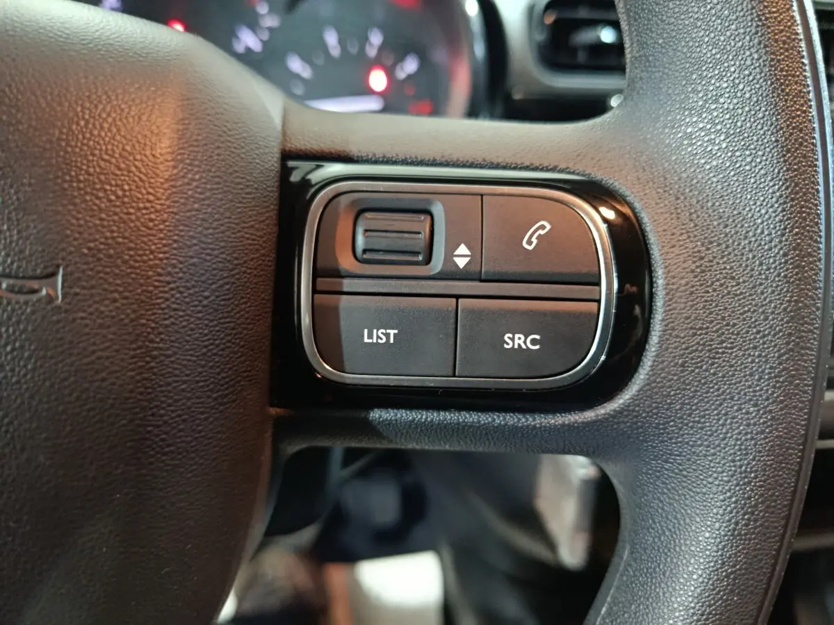 Gros plan sur les commandes gauche du volant noir de la Citroën C3 2024, boutons LIST, SRC et téléphone visibles.