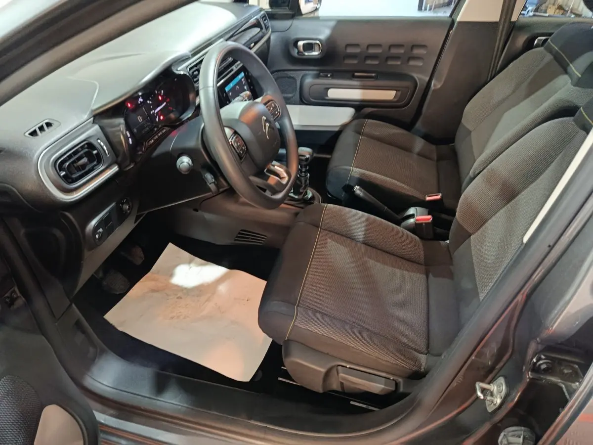 Vue intérieure côté conducteur de la Citroën C3 gris foncé 2024, avec tableau de bord numérique et sièges tissu noirs.