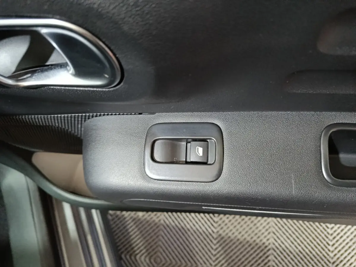 Gros plan sur le bouton de commande de la vitre électrique côté conducteur dans une Citroën C3 gris foncé, intérieur noir.
