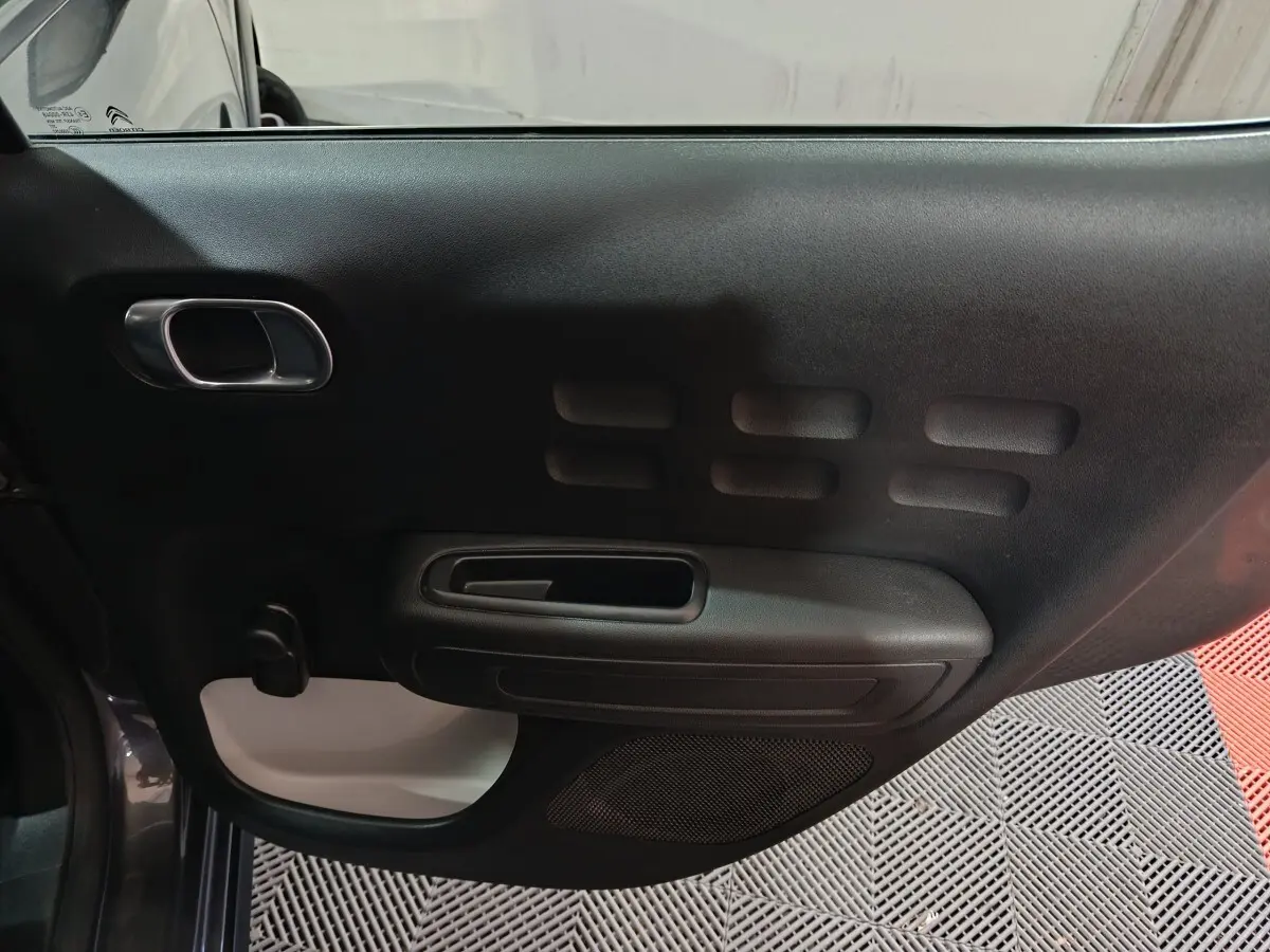 Vue intérieure de la porte côté conducteur de la Citroën C3 gris foncé, avec poignée intégrée et panneau noir texturé.