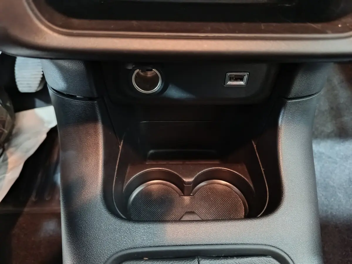 Gros plan sur la console centrale de la Citroën C3 2024 gris foncé, montrant prise 12V, port USB et porte-gobelets.
