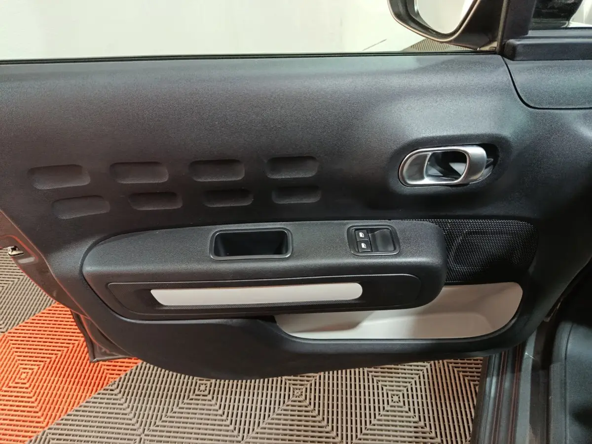 Vue intérieure de la porte côté conducteur d'une Citroën C3 gris foncé, avec commandes de vitres et poignée argentée.